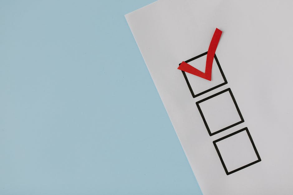 A white sheet of paper on a light blue background displays a vertically arranged checklist with three empty boxes, one of which has a bold, red checkmark inside it. The checkmark appears to be made from a red paper cutout or marker, placed diagonally within the top box. The paper and checklist boxes are positioned near the top right corner of the image, with the rest of the blue background mostly empty, creating a clean and minimalistic scene. This visual could relate to planning or completing a house removal checklist, such as packing, moving schedules, or task management, integral to home relocation logistics. Occasionally, Ilford Man and Van's removals services might assist with the organisation and execution of such checklists during furniture transport and packing processes in house moves, emphasizing careful planning and thorough execution in moving services.